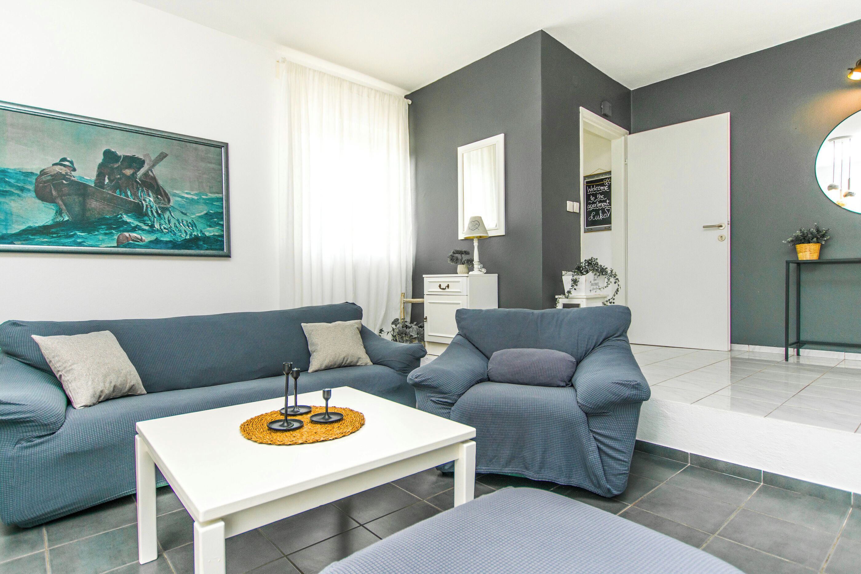 A living room with a sofa, a coffee table, a painting, a mirror, and a door leading to another room.