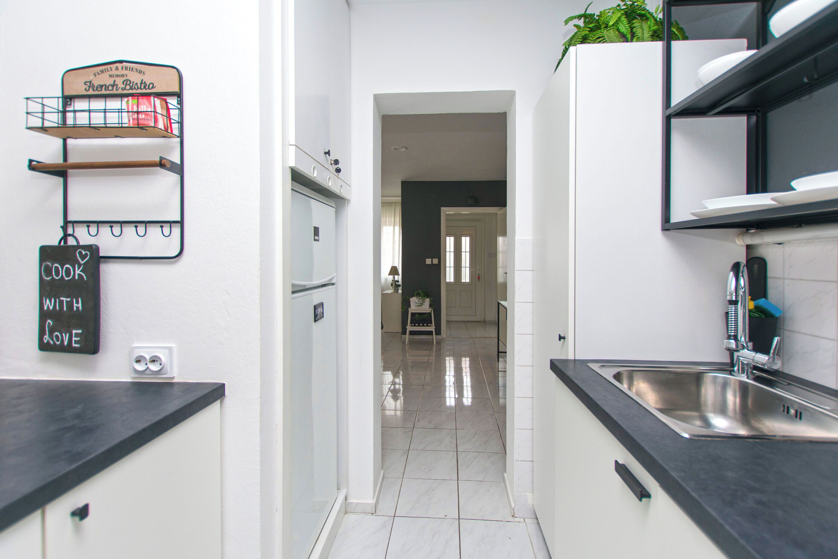 Una cocina estrecha con mostrador negro, un lavamanos de acero inoxidable y un cartel de pizarra.