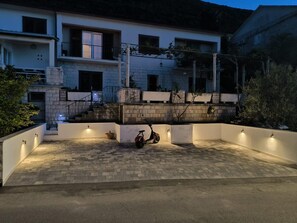 A modern building with a paved courtyard, a scooter, and a stone wall. - Apartments Ivana (Trpanj)