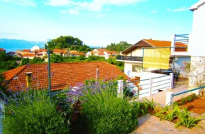 A residential area with terracotta-tiled roofs, a white building with a balcony, and a garden with lavender. - Apartments Ivana (Trpanj)
