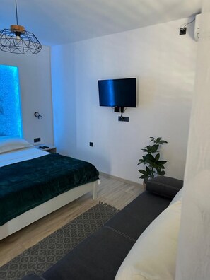 A modern bedroom with a bed, a TV mounted on the wall, a bedside table, a plant, and a window with blue lighting. - Apartments Ivana (Trpanj)