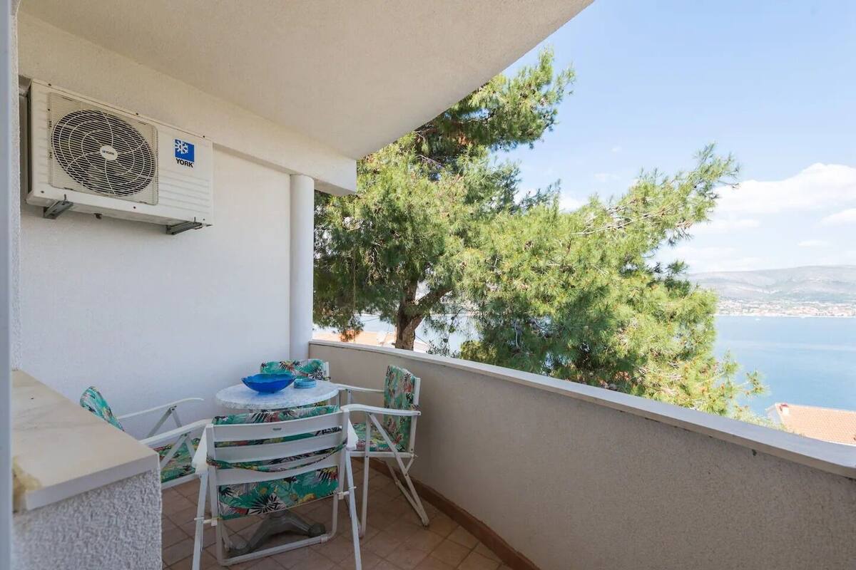 A balcony with a table and chairs, overlooking a body of water and a distant cityscape.