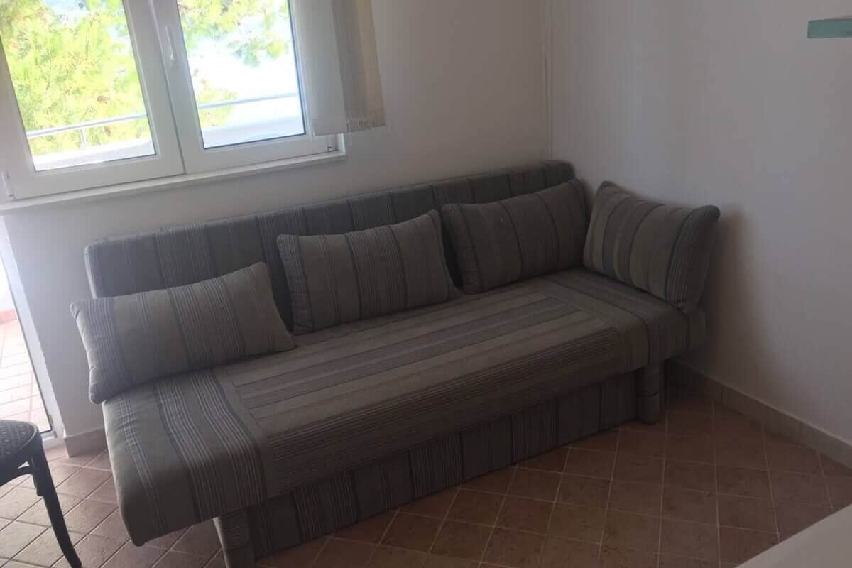 A corner sofa with a striped pattern, positioned next to a window with a view of greenery outside.