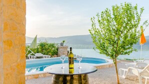 Ένας χώρος δίπλα στην πισίνα με ένα στρογγυλό τραπέζι, ένα μπουκάλι κρασί και ξαπλώστρες.