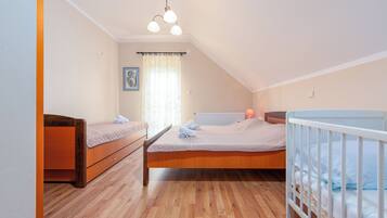 Een slaapkamer met een houten vloer, een bed met een wit hoofdeinde, een houten dressoir en een wit babybedje.