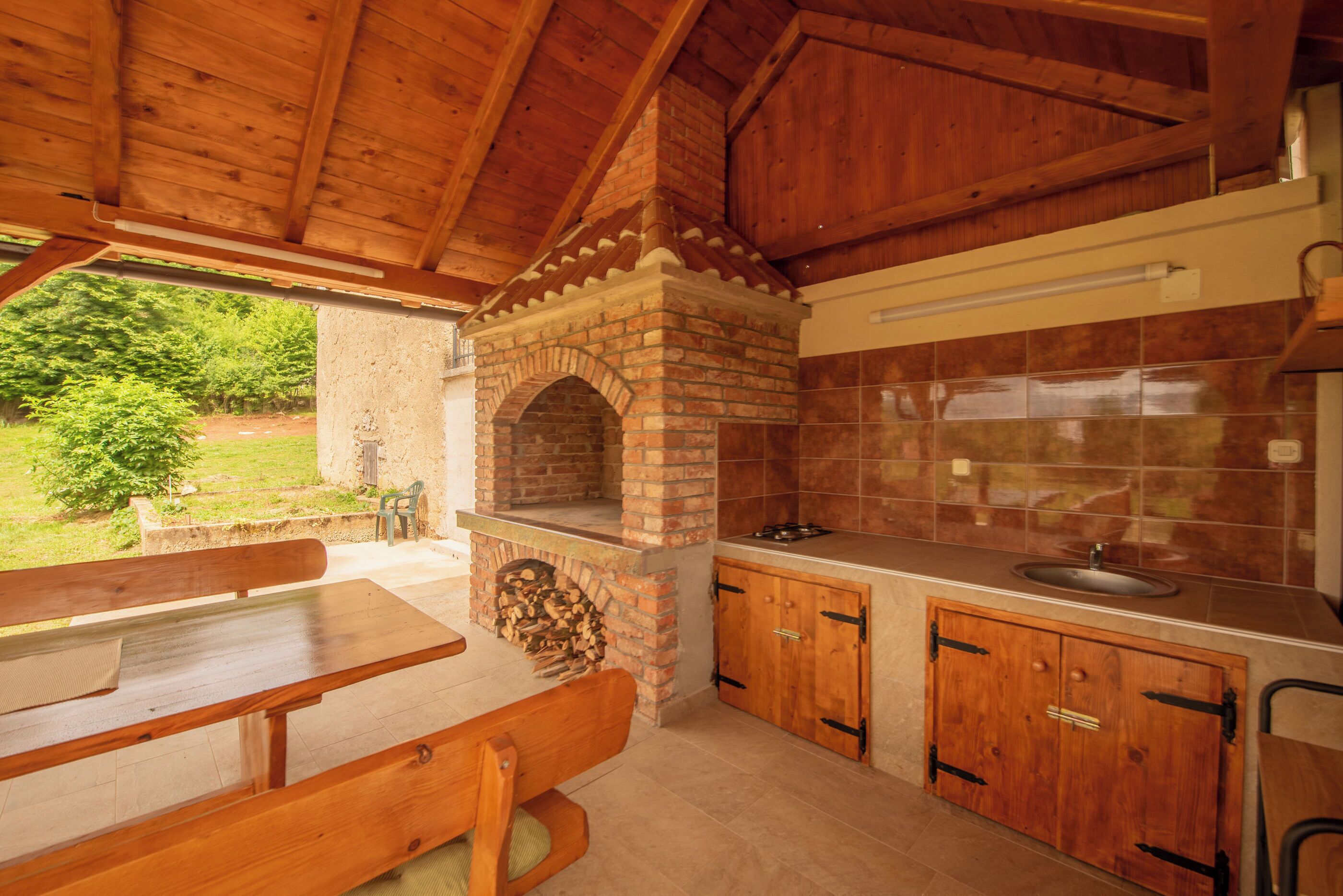 Cocina exterior con horno de ladrillo, armarios de madera y un banco.