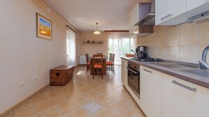 A compact kitchen with a dining area, featuring a built-in oven, a coffee maker, and a small cabinet. - House Rose (Otocac)