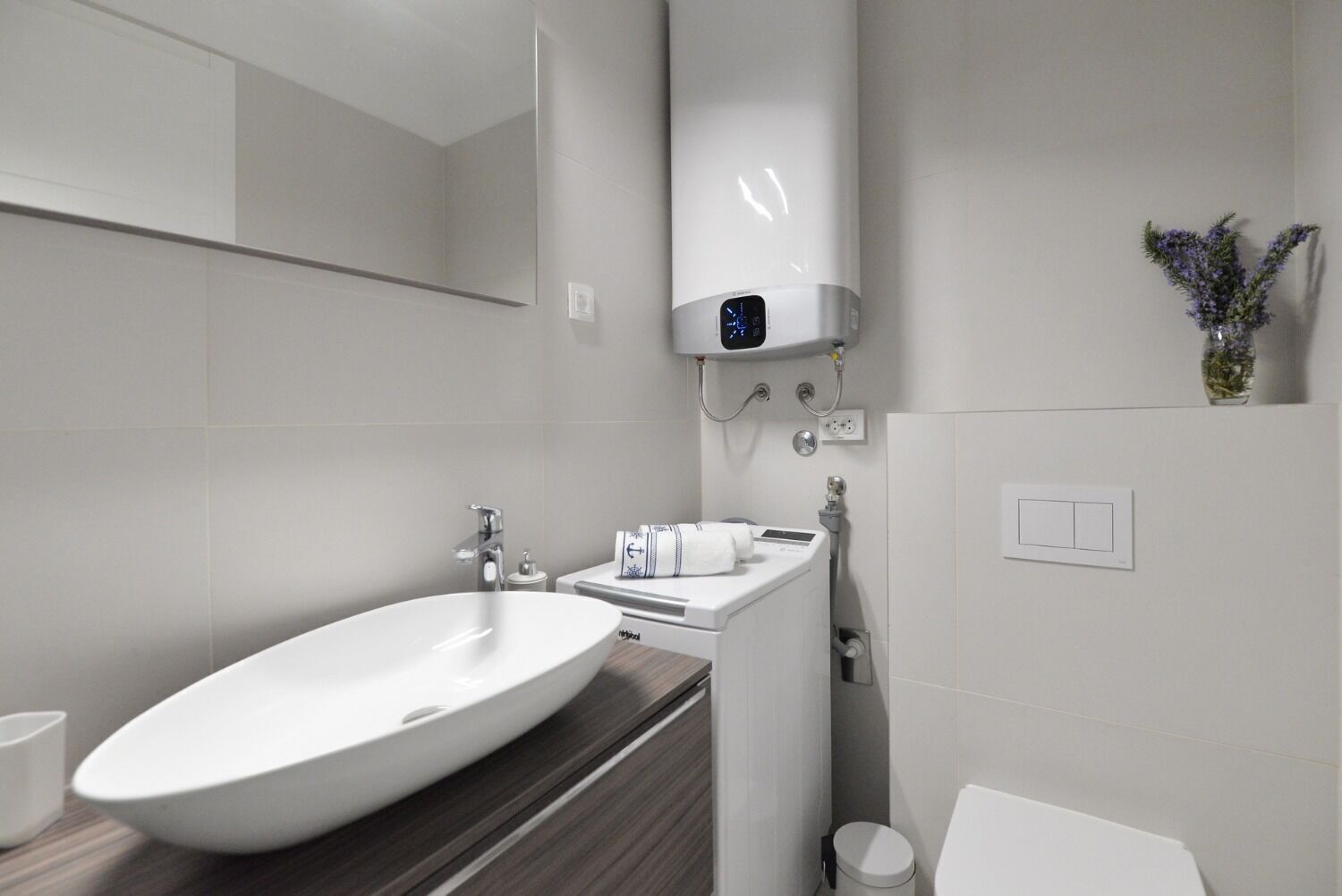 Une salle de bain moderne avec un grand lavabo ovale, un miroir, un distributeur de serviettes et des toilettes.