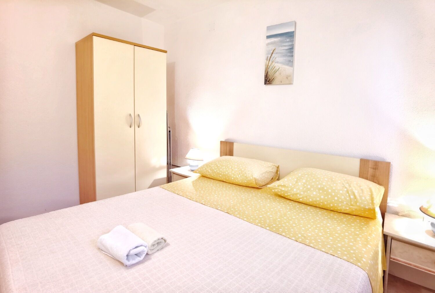 A bedroom with a bed, a wardrobe, a nightstand, and a wall art piece.
