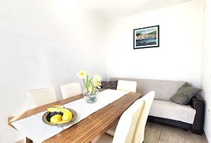 Ein Essbereich mit einem Holztisch, weißen Stühlen, einer Blumenvase und einem gerahmten Bild an der Wand.