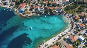 Eine Luftaufnahme einer Küstenstadt mit klarem türkisblauem Wasser, Booten und Gebäuden mit roten Ziegeldächern.