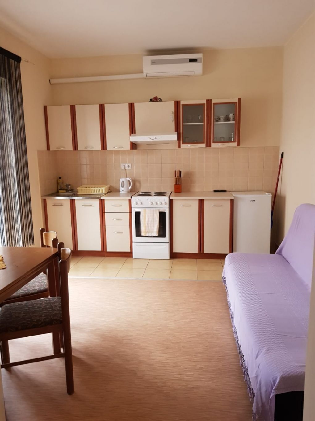A compact kitchen with a stove, oven, and cabinets. There is a dining table with chairs and a purple sofa.