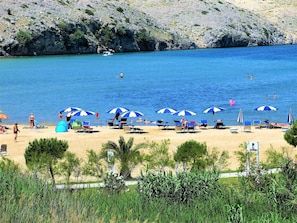 Una spiaggia con numerosi ombrelloni e lettini, una costa rocciosa e alcune persone che nuotano.