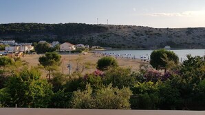 A coastal view with a beach, a hill with sparse vegetation, and buildings in the background. - Apartment Mari (Lopar)