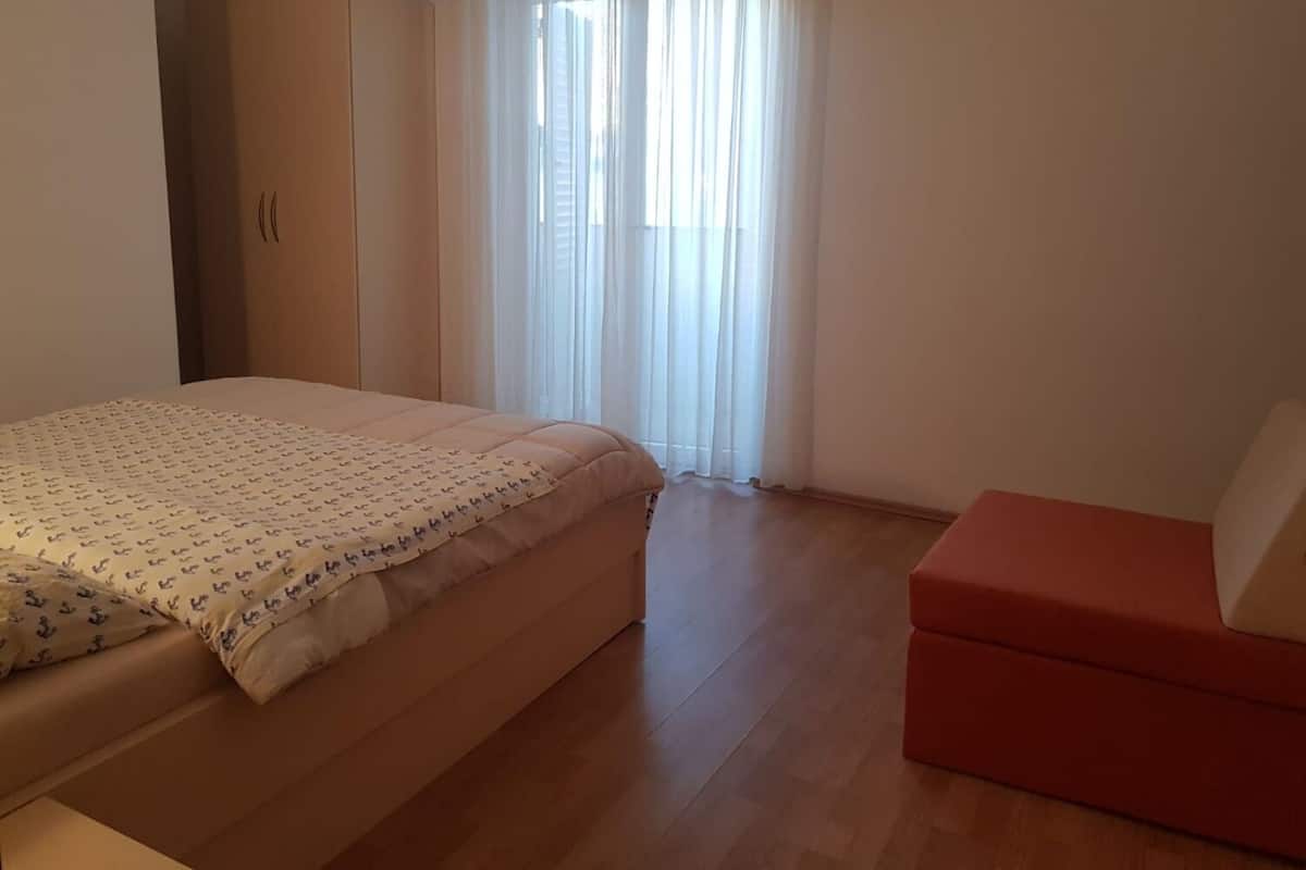 A bedroom with a bed, a wardrobe, a window with curtains, and a red bench.