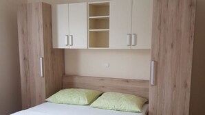 A bedroom with a bed, two green pillows, and a wooden wardrobe with a shelf above the bed. - Apartment Mari (Lopar)