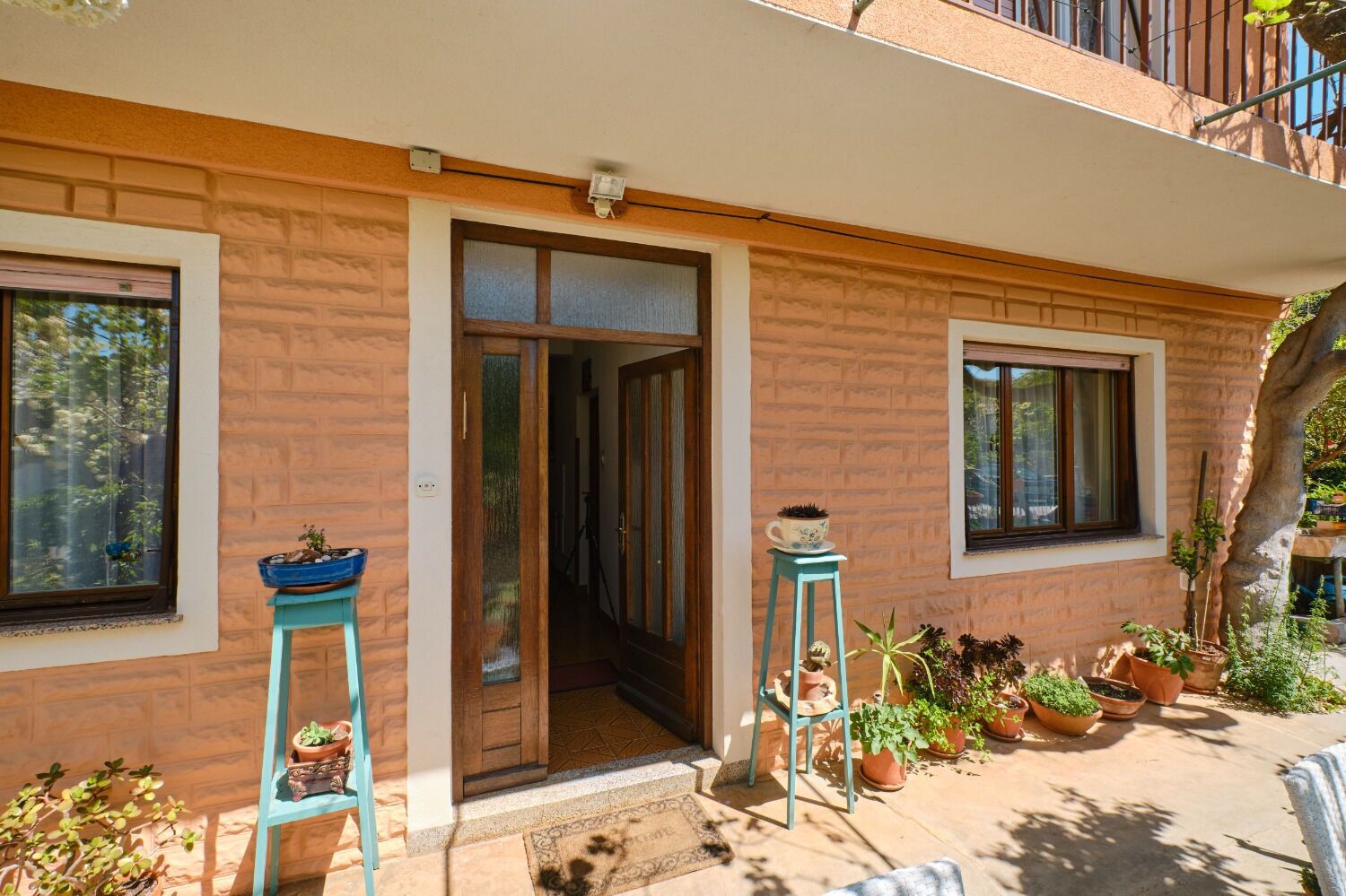 Un immeuble d’habitation avec une porte en bois, deux fenêtres et un balcon agrémenté de plantes en pot.