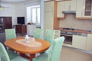 Un espace repas comprenant une table ronde, des chaises, un téléviseur et une cuisine équipée de placards et d’appareils électroménagers.