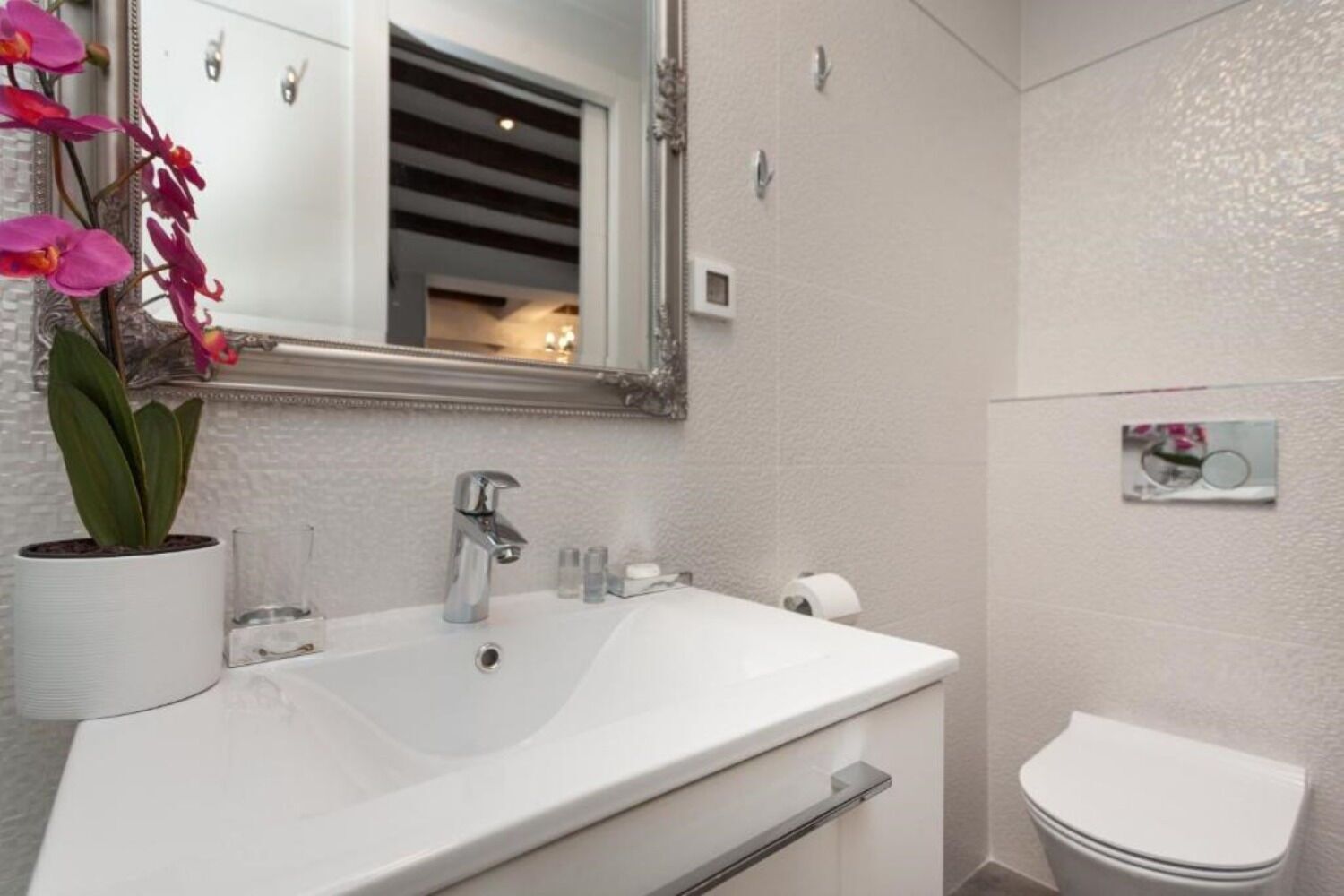 A bathroom with a white sink, a mirror, a toilet, and a potted orchid.