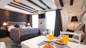 A modern hotel room with a bed, bedside tables, a dining area with breakfast, and a TV. - Apartments Regent 2 (Rovinj)