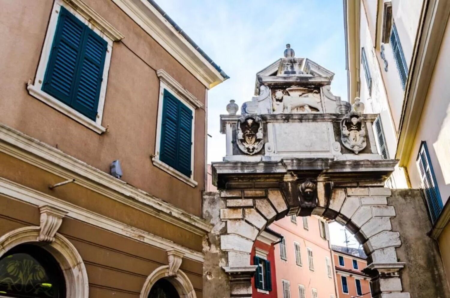 A street view with a building featuring a classical archway and a statue on top.