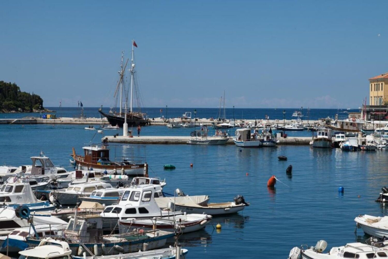 A marina with various boats docked, a pier with people, and a building in the background.
