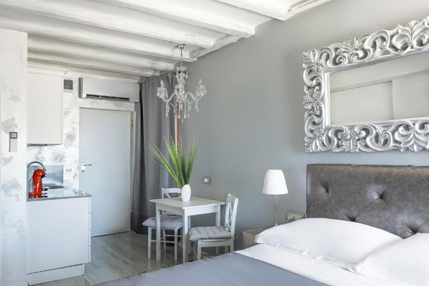 A compact hotel room with a bed, a dining area, and a kitchenette.