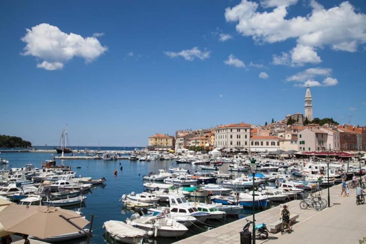 Un puerto deportivo con numerosas embarcaciones amarradas, una torre destacada y edificios con tejados de tejas rojas.
