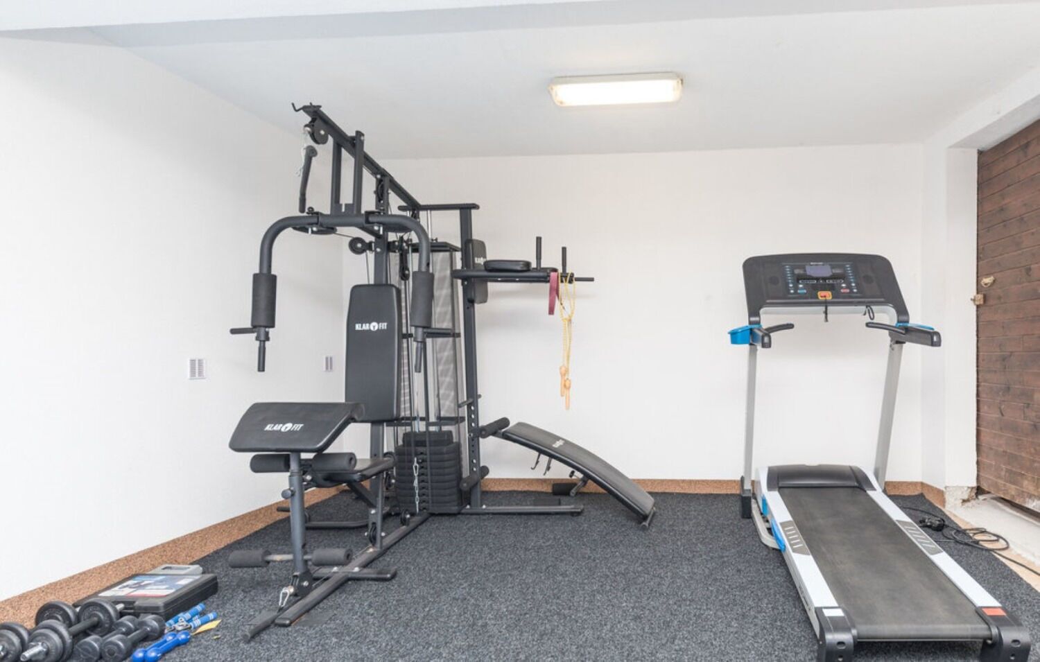 Une salle de sport à domicile équipée d’un banc de développé couché, d’un support à squats, d’un tapis de course et d’haltères.