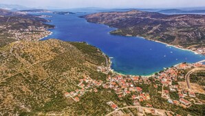 Vista aérea de un pueblo costero con un puerto deportivo, rodeado de colinas y una gran masa de agua.