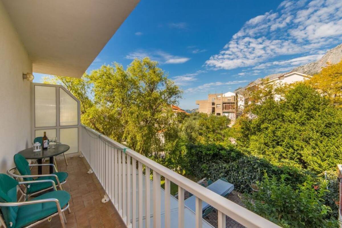 En balkon med et bord og stole, der vender ud mod en have og bygninger.