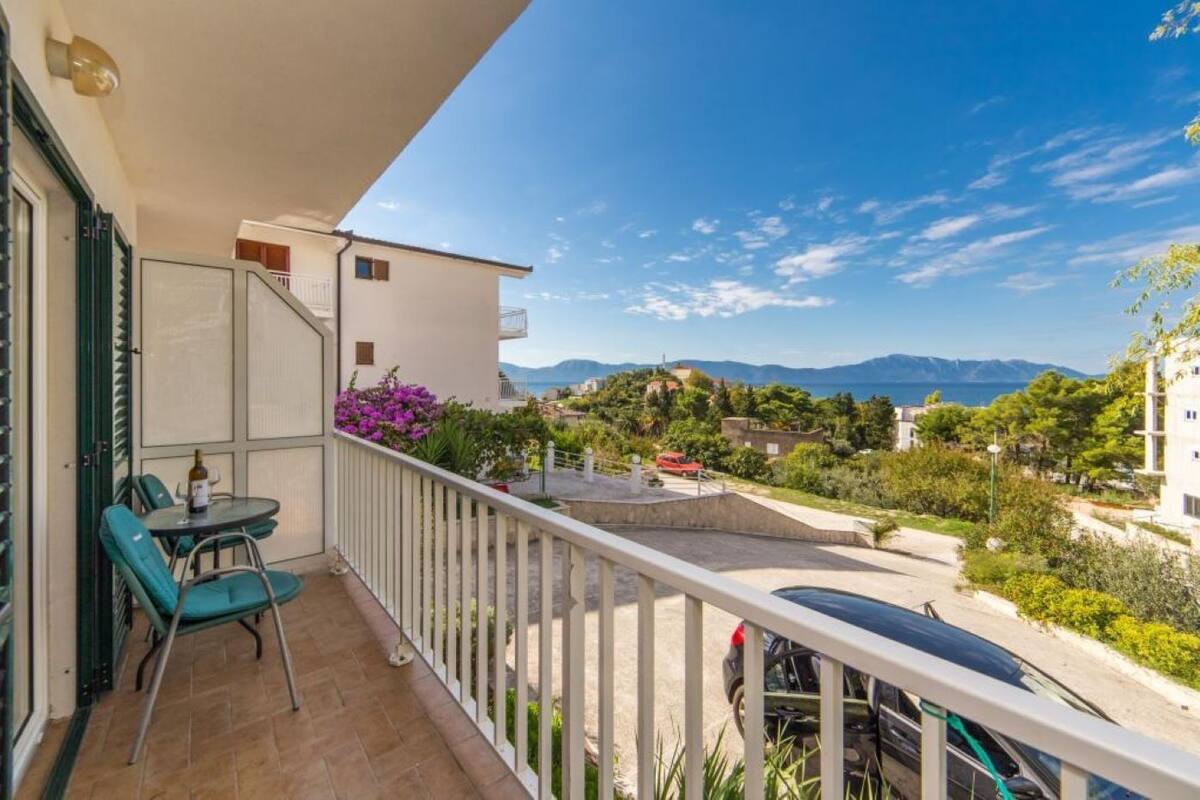 En balkon med et bord og stole, der udover et boligområde med huse og en klar himmel.
