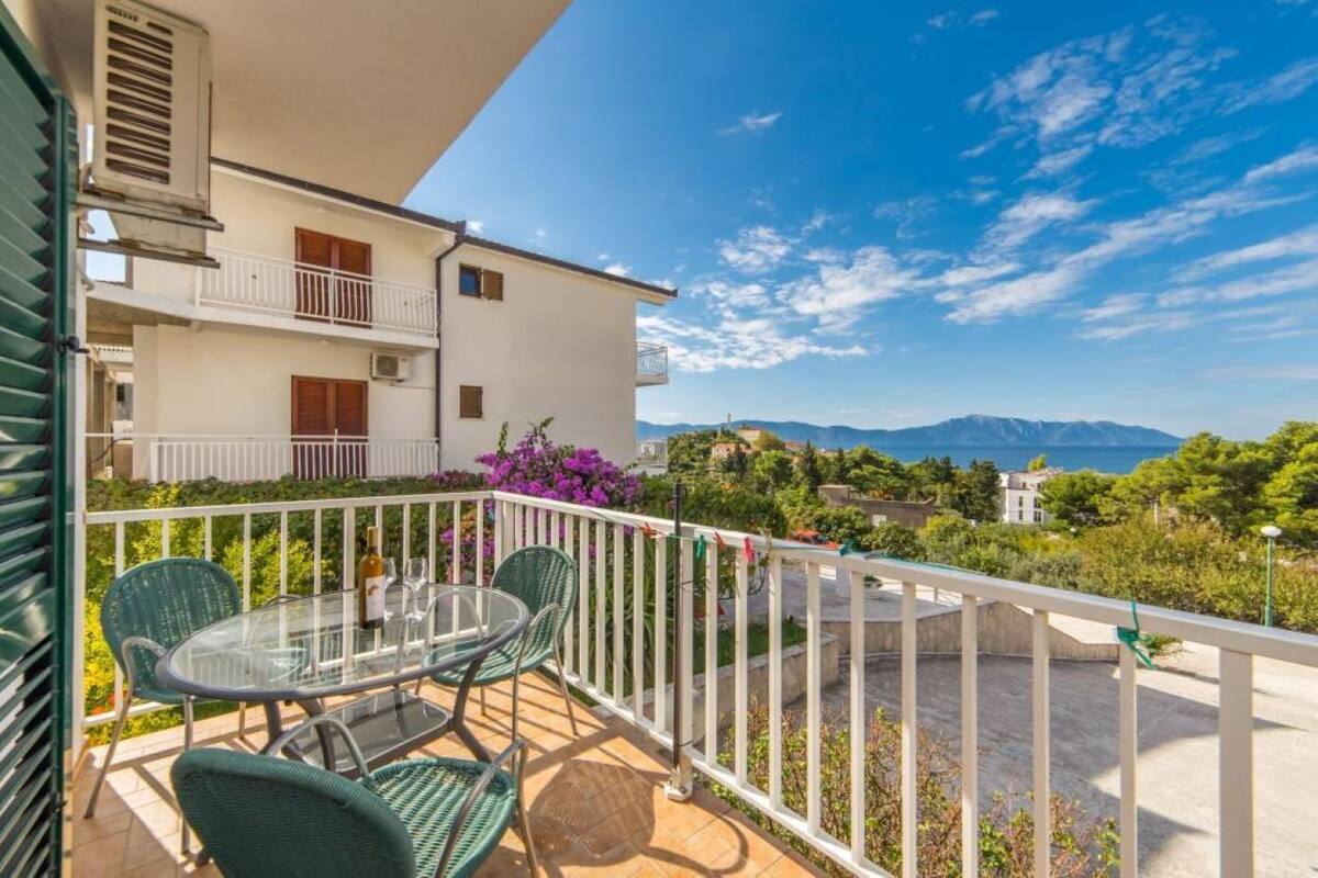 En balkon med et bord og stole, der giver udsigt over et smukt landskab med bjerge og vand.