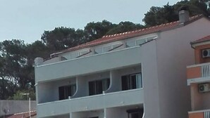Um edifício com vários andares, varandas, fachada de pedra e estacionamento com carros.