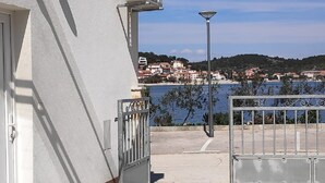 A building with a white exterior, a metal gate, and a view of a body of water and a town in the background. - Apartment Tona (Tisno)