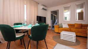 A dining area with a table, chairs, and a TV. There is a sofa and a mirror in the living area. - Apartments Bionda (Sibenik)