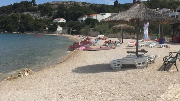 A beach with a thatched umbrella, lounge chairs, and a rocky shoreline. - Apartments Bionda (Sibenik)