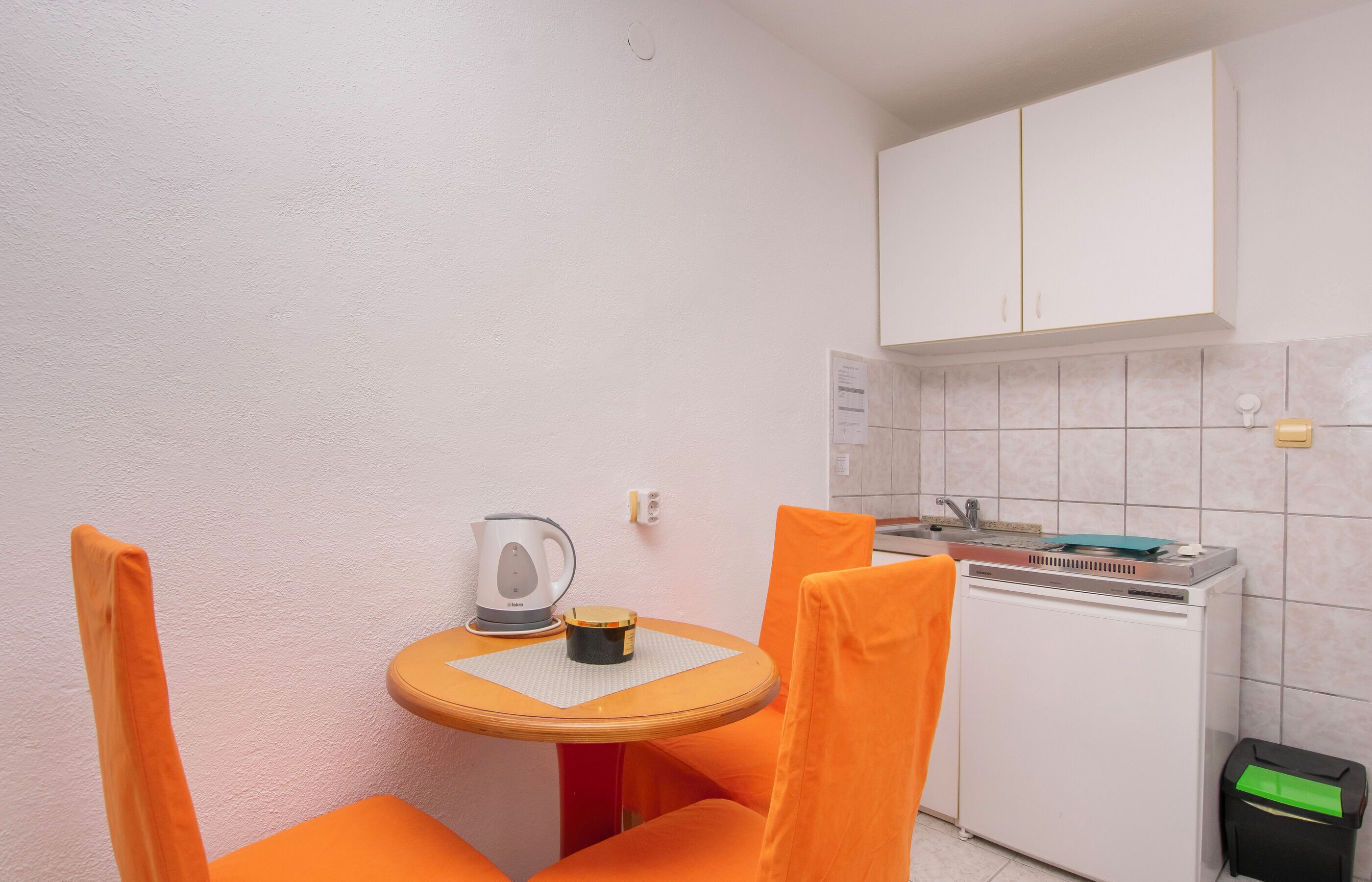 A compact kitchen with a small table and chairs, a kettle, and a sink.