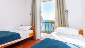 A hotel room with two beds, a balcony with a view of the sea, and a window with curtains. - Apartments Zorica (Omis)