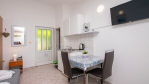 A compact kitchen with a dining table, chairs, a TV mounted on the wall, and a small cabinet. - Apartments Zorica (Omis)