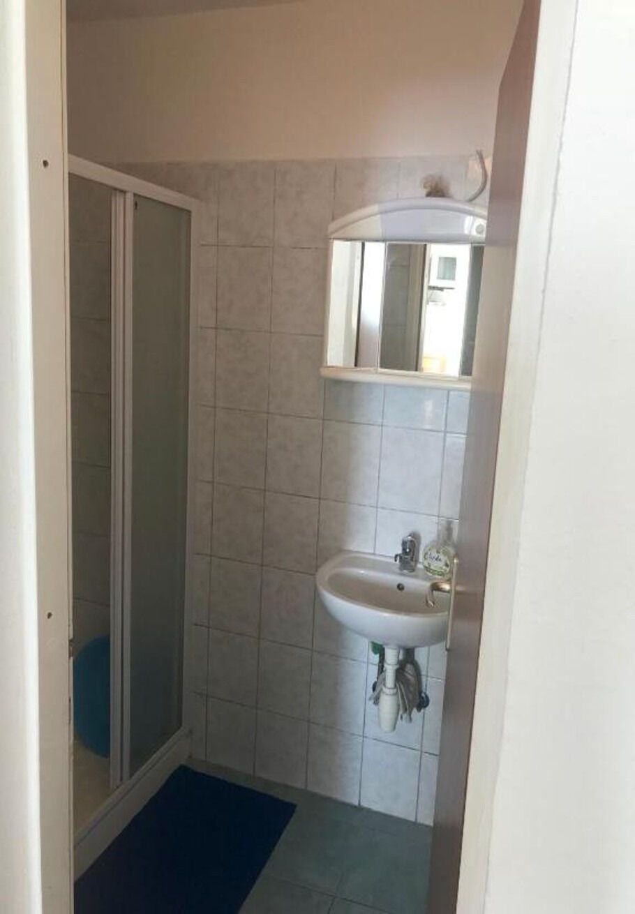 Pieni kylpyhuone, jossa on suihku, pesuallas ja peili.