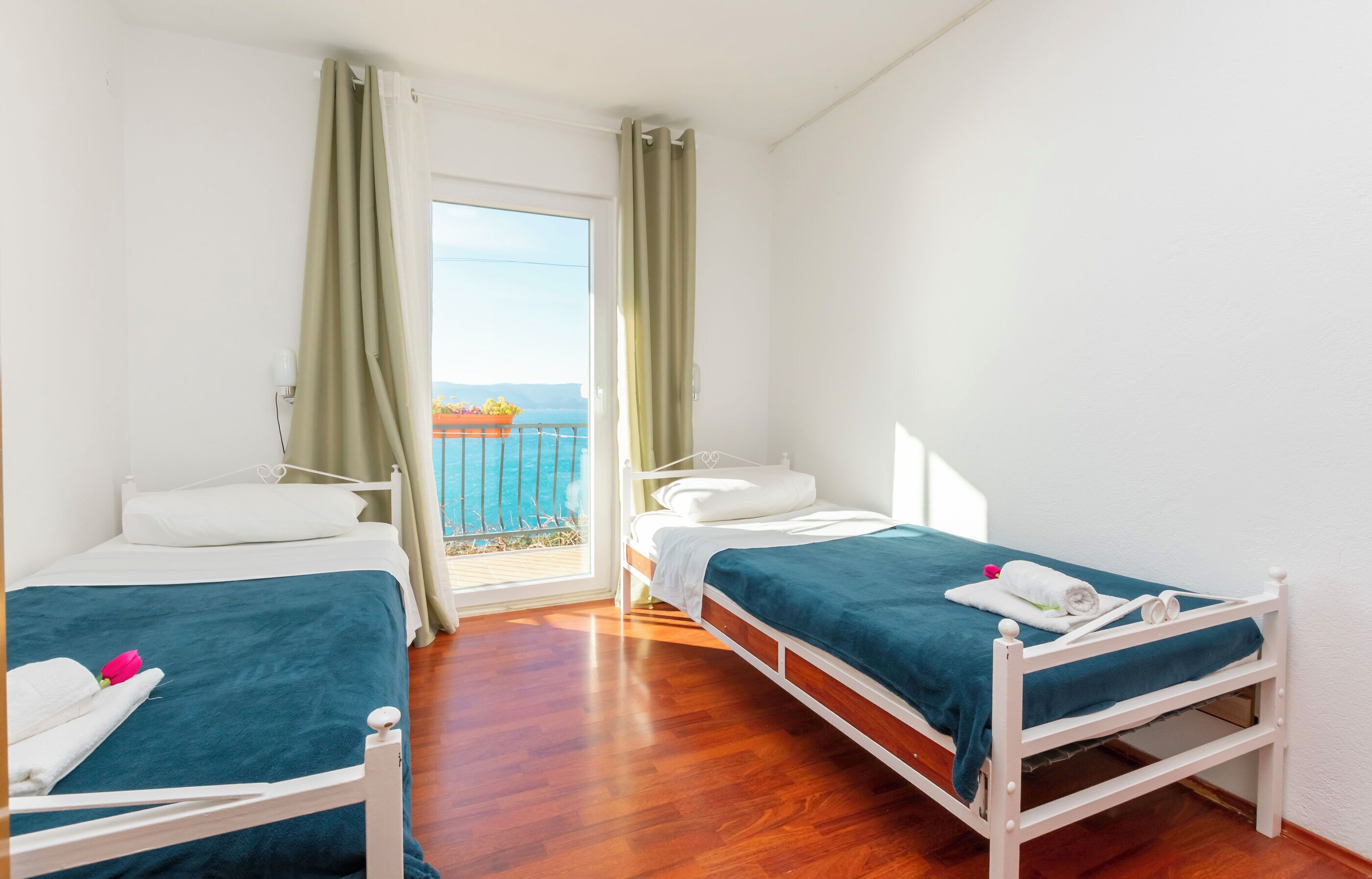 Ein Hotelzimmer mit zwei Einzelbetten, einem Balkon mit Meerblick und einem Fenster mit Vorhängen.