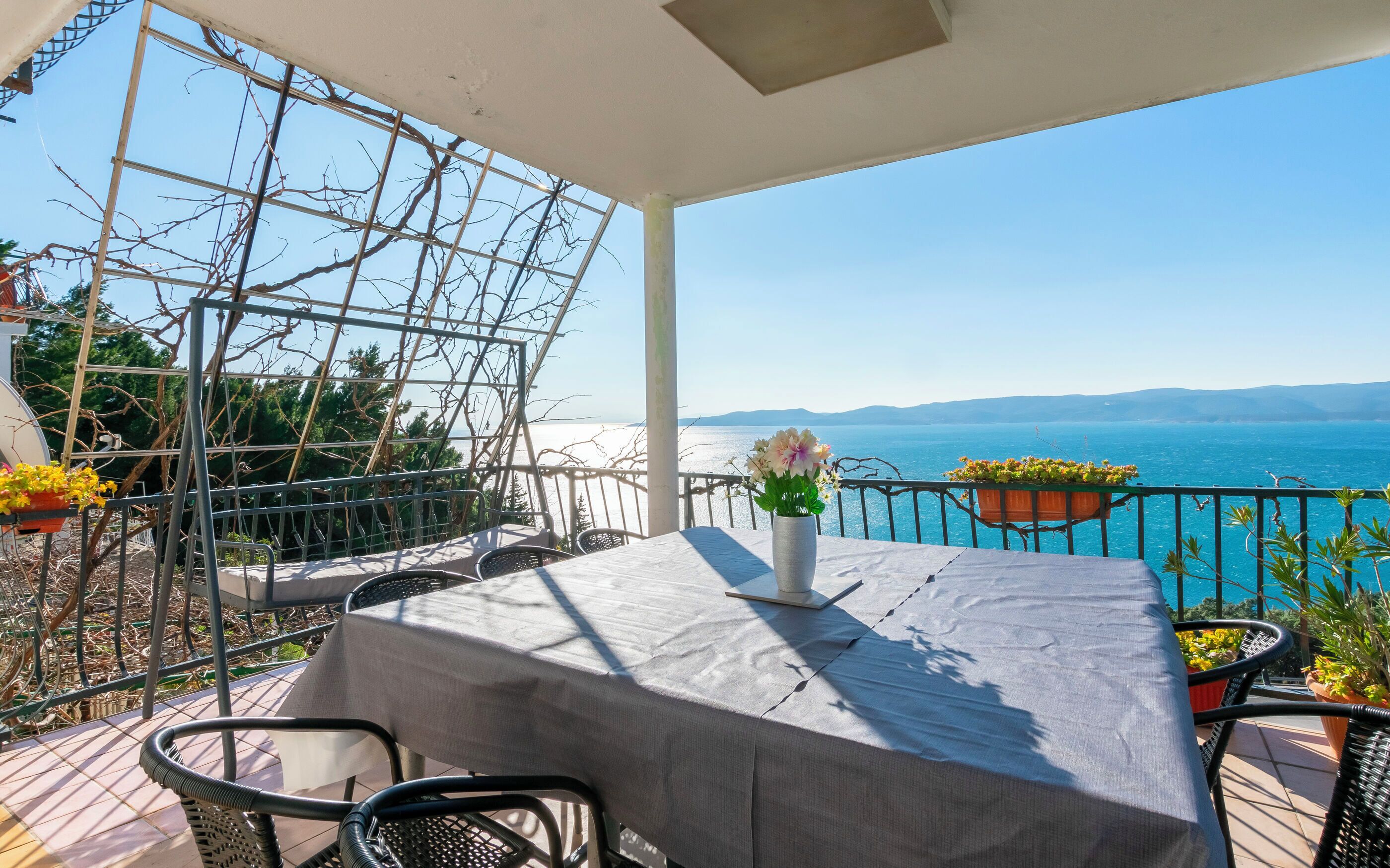 Eine Terrasse mit Tisch und Stühlen, einem Blumentopf und Blick auf das Meer.