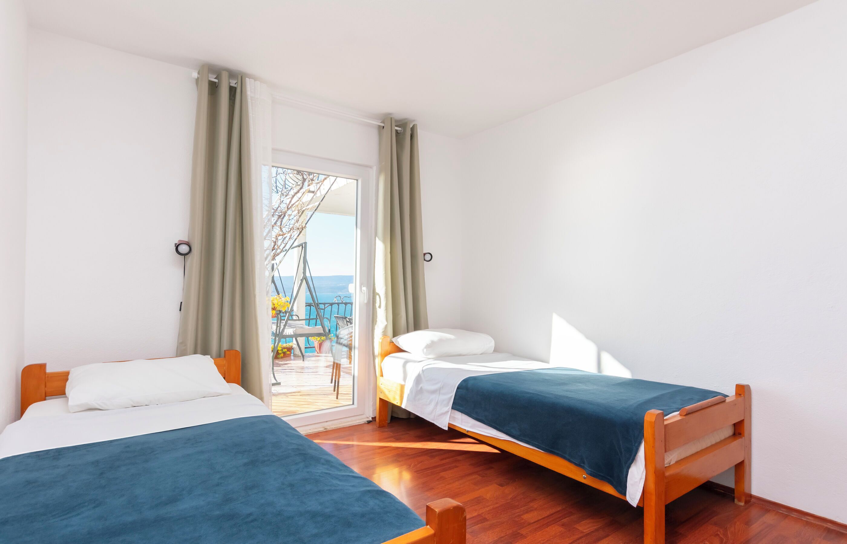 A room with two wooden beds, a balcony with a view, and a door leading outside.