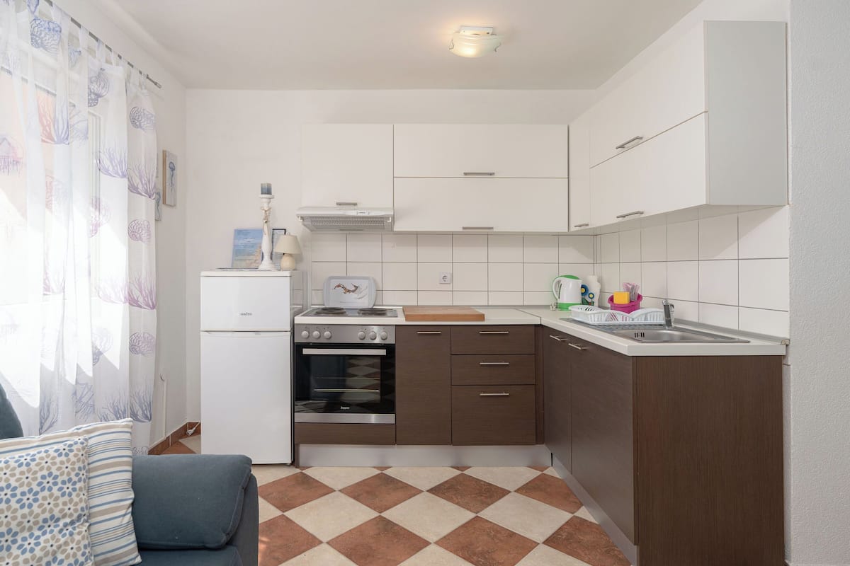 Una cucina compatta con piano cottura, forno e lavello. C'è un'area pranzo con una sedia e un tavolo.
