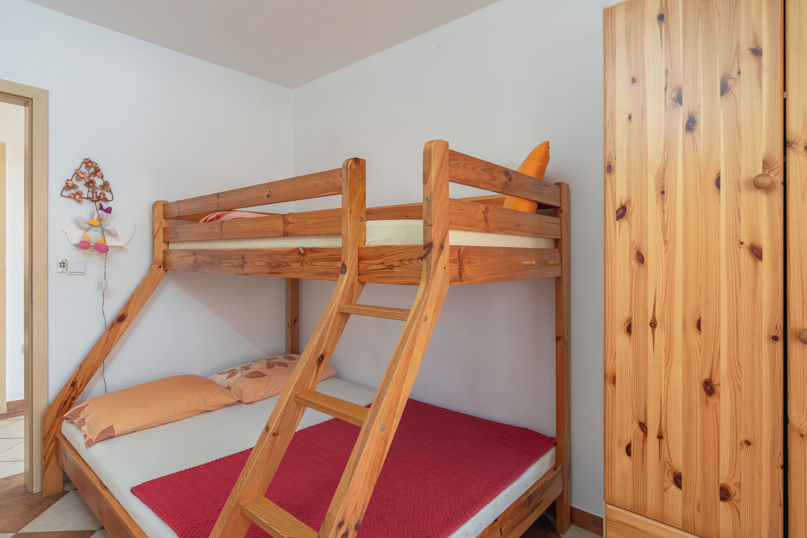 A bunk bed with a ladder, a wardrobe, and a wall decoration.