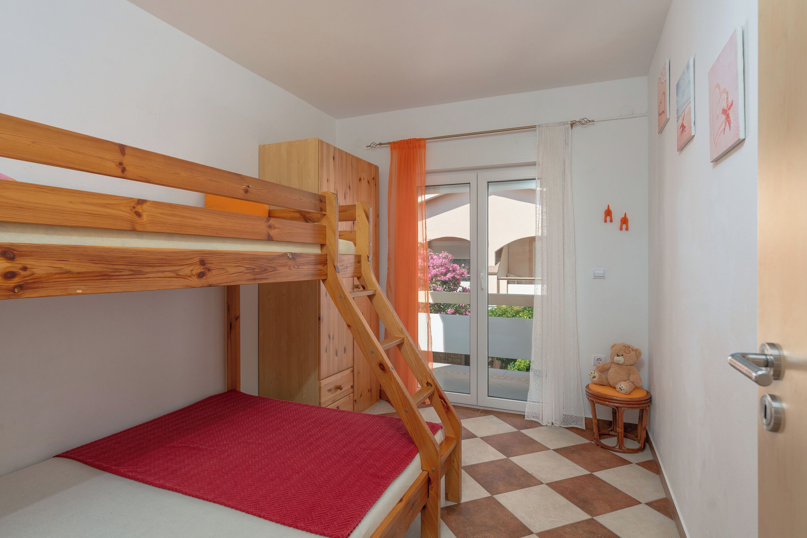 A bedroom with a bunk bed, a small table with a teddy bear, and a view of the outside balcony.