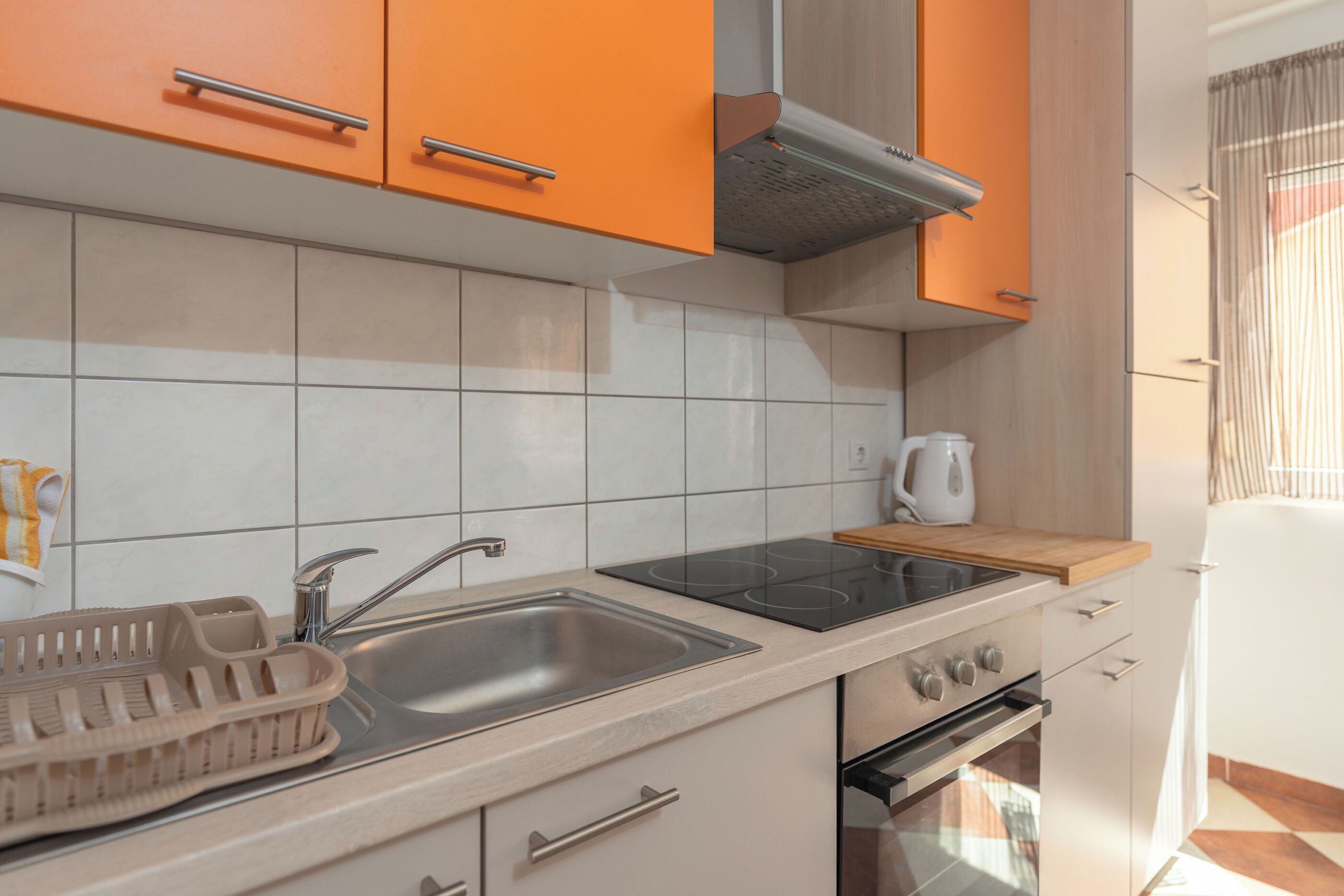 Una cocina con azulejos blancos, horno, estufa y armarios color naranja.