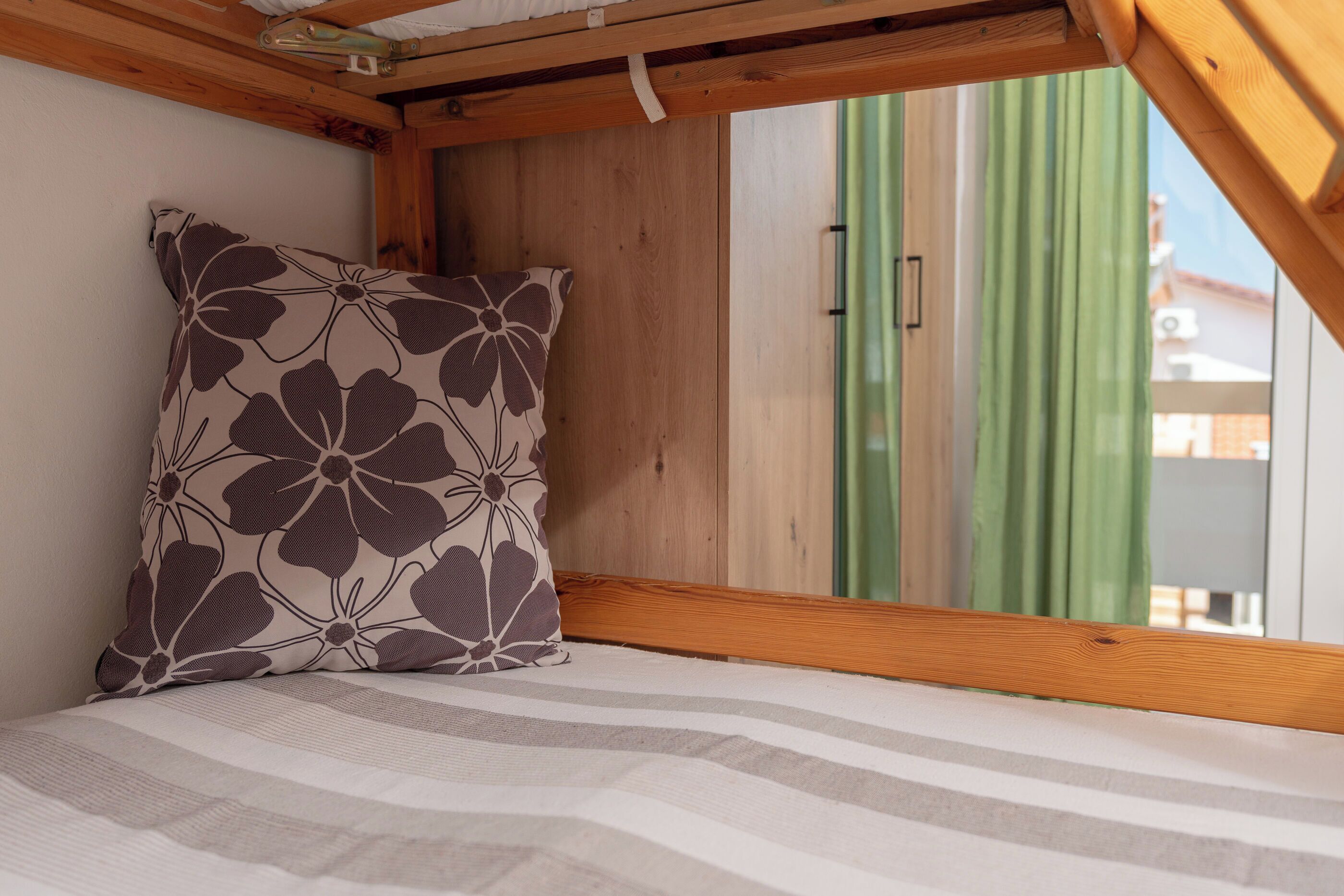 A small, cozy room with a wooden ceiling and a window with green curtains.