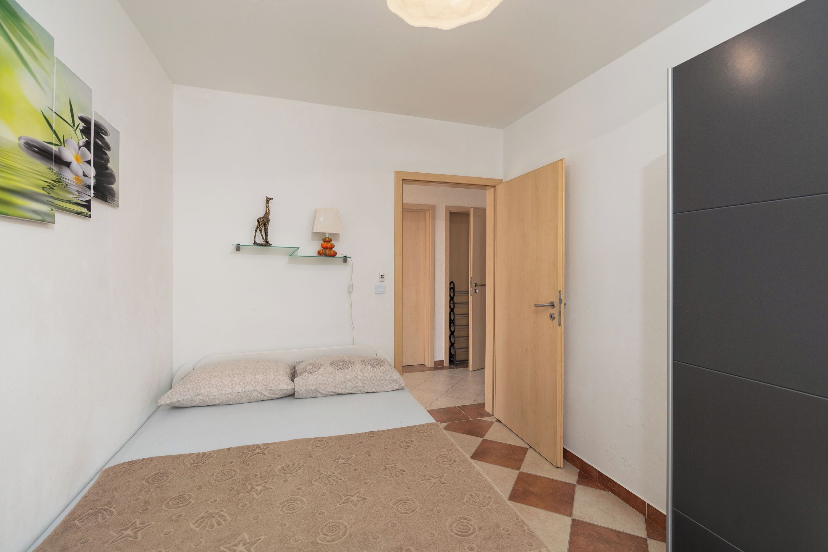 Un dormitorio con cama, mesita de noche, lámpara y estante con adornos.
